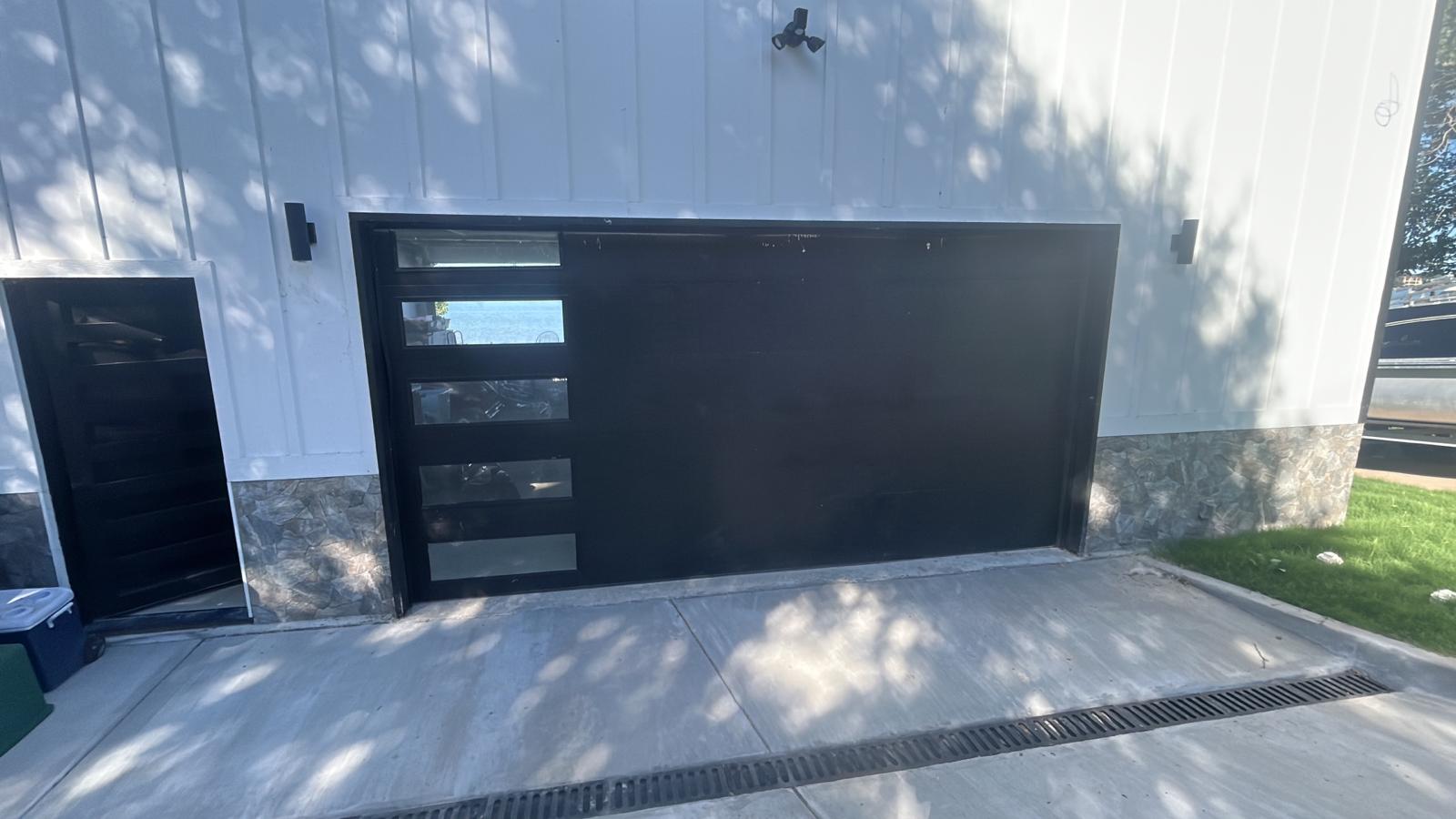 Modern black flush-panel garage door with stacked vertical windows on a white board-and-batten home